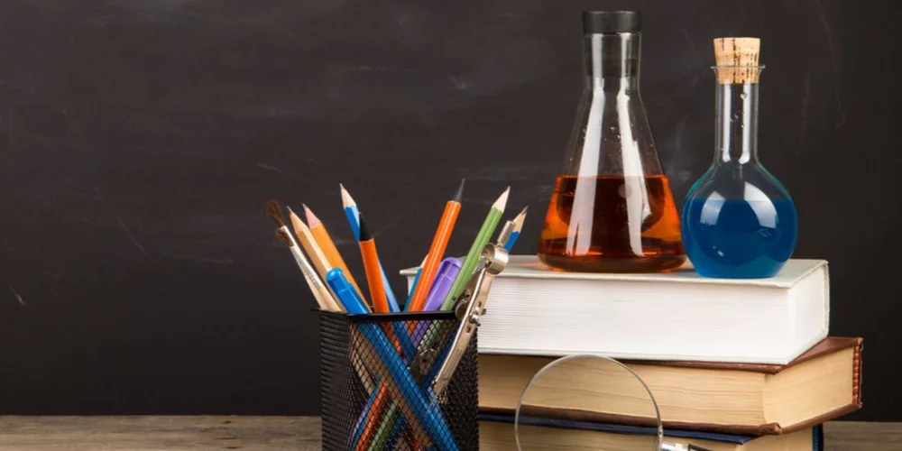 Laboratory flasks with colorful liquids atop stacked books, emphasizing education and experimentation.